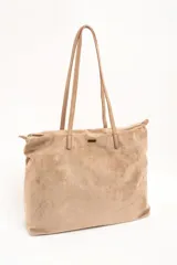 Bolso tipo shopper de gamuza vegana color tostado, con doble asa larga para hombro y cierre superior. Cuenta con una pequeña placa metálica con el logo de la marca en la parte frontal.