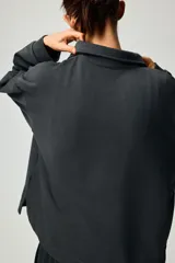 Buzo en tejido liviano color gris oscuro, con cuello camisero, tapeta de botones, hombros caídos y puños acanalados.