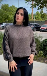 Blusa de tejido de punto en color gris, con cuello redondo y mangas largas que presentan un detalle de encaje negro a lo largo de los brazos.