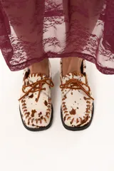 Zapato náutico de horma cuadrada confeccionado en cuero de pelo de vaca con estampado animal print. Presenta detalles de pasamanería en cuero descarne en el frente y laterales, cordones frontales y suela plana con pequeño taco.