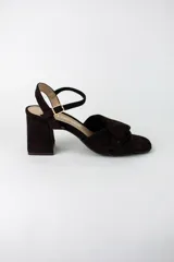 Sandalia de tacón cuadrado medio, confeccionada en material textil tipo gamuza color negro. Presenta un diseño de tiras cruzadas con nudo en la parte delantera y una tira ajustable con hebilla metálica en el tobillo.