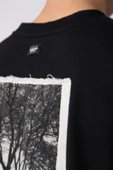 Remera de corte oversize confeccionada en algodón premium de gramaje pesado, color crudo. Presenta un bordado frontal pequeño en el centro del pecho con un diseño de dos árboles unidos por sus raíces y un parche estampado en la espalda con una silueta de mano fusionada con ramas.