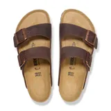 Sandalia Birkenstock modelo Arizona de dos correas ajustables con hebillas metálicas. Presenta una capellada de cuero engrasado color marrón y una plantilla anatómica de corcho con suela de goma.