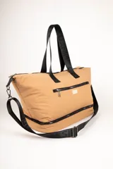 Bolso de gran capacidad color beige, con asas fijas superiores y correa de cinta negra desmontable y regulable. Presenta un bolsillo externo con cierre, un compartimento inferior con cierre y logo de la marca Daniel Cassin en el frente.