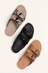 Sandalias de cuero color negro con dos tiras anchas sobre el empeine, cada una con hebillas metálicas ajustables y detalles de tachas plateadas. La suela es de cuero con un borde de color madera.