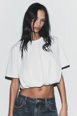Camiseta cropped blanca de algodón 100%, con cuello redondo, manga corta y bajo abullonado con pliegues.