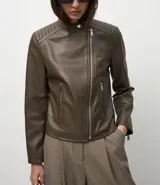 Campera biker de poliuretano color verde oliva, con cierre frontal asimétrico, bolsillos laterales con cremallera y detalle capitoneado en los hombros.
