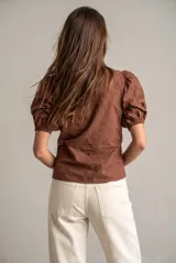 Blusa marrón de algodón con bordados sutiles, escote en V, mangas cortas abullonadas y detalle de fruncido con cordón ajustable en el centro del frente.