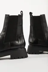 Bota tipo Chelsea de cuero negro con paneles elásticos laterales y suela track dentada de goma.