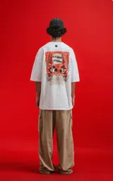 Remera blanca de algodón premium con cuello redondo y calce oversize. Presenta un pequeño estampado en el pecho izquierdo de Mickey Mouse en una pose dinámica sobre un fondo naranja.