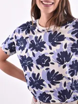Remera de mangas cortas con estampado de flores abstractas en tonos azul y lila sobre fondo blanco.