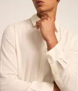 Camisa de manga larga color crema, con cuello inglés, abotonada y textura de rayas verticales.