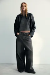 Camisa de efecto piel en color negro, con cuello solapa, manga larga y bolsillos de plastrón en el delantero. Presenta cierre frontal con botones ocultos por tapeta.