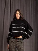 Buzo corto de tejido de punto en color negro, con diseño de textura en relieve y líneas horizontales blancas. Presenta cuello redondo y mangas largas con puños ajustados.