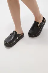 Suecos negros de estilo zueco con capellada de cuero sintético, detalle de hebilla metálica dorada y tachas decorativas alrededor de la suela. Poseen plantilla ergonómica y suela de plataforma dentada.