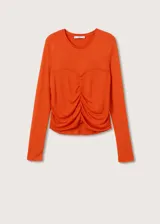 Camiseta de manga larga color naranja, con cuello redondo y diseño entallado. Presenta un detalle fruncido central y costuras decorativas en el frente.