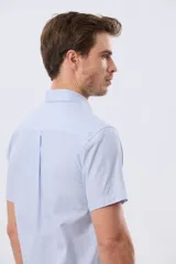 Camisa de manga corta a rayas celestes y blancas, con cuello abotonado, bolsillo frontal con logo bordado y cierre frontal de botones.