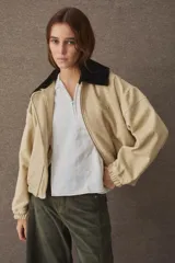 Campera tipo bomber de paño color beige, con cuello de piel sintética negro desmontable, cierre frontal y puños elásticos. Presenta logo bordado en el frente y bolsillos laterales.