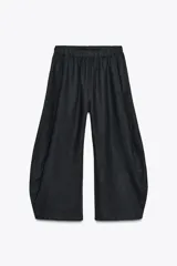 Pantalón de tiro alto color negro, confeccionado en tejido con lino. Presenta cintura elástica ajustable con lazada interior y bolsillos laterales. El bajo tiene un acabado con volumen pronunciado.