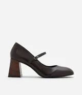 Zapato estilo Mary Jane de poliuretano color marrón oscuro, con punta redondeada, tira con hebilla ajustable sobre el empeine y taco bloque de altura media con acabado símil madera.