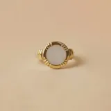 Anillo de diseño circular con centro de nácar y borde texturizado en tono dorado, montado sobre una banda de plata.