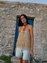 Pollera corta de diseño escalonado confeccionada en rafia con flecos largos que aportan movimiento. Presenta una estructura versátil que permite su uso también como top.