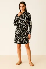 Vestido corto tipo camisa, de manga larga, con cuello y botones frontales. Presenta un estampado abstracto en blanco sobre fondo negro.