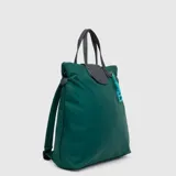 Mochila convertible en tote bag de diseño minimalista, color verde oscuro con acabado impermeable. Cuenta con asas superiores y detalles en cuero sintético gris, cierre superior y un llavero decorativo con la letra B en color turquesa.
