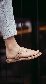 Sandalia plana de cuero color beige, con diseño de tira ancha decorada con tachas metálicas doradas y oscuras, y suela baja acolchada.