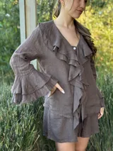 Camisa de lino azul marino con volados en cascada a lo largo del frente y en los puños de las mangas largas. Presenta un escote en V con un botón de nácar visible.