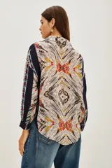 Camisa de manga larga con estampado étnico multicolor, cuello clásico y cierre frontal con botones. Presenta un diseño de rayas verticales con patrones geométricos y detalles en tonos azules, rojos, amarillos y beige.