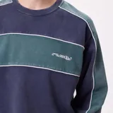 Buzo de cuello redondo Rusty con diseño de bloques de color en azul marino y verde, con detalles de líneas blancas y logo bordado en el pecho.