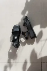 Sandalias de plataforma color negro, con diseño de dos tiras anchas en el empeine y cierre con velcro en el tobillo. Presentan una suela de plataforma alta y liviana.