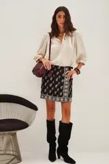 Falda corta negra estilo wrap con estampado paisley en tonos rojo y blanco. Presenta un borde decorativo con motivos circulares en tonos plateados y beige.