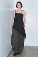 Top negro con estampado de lunares blancos, escote recto, tirantes finos, detalle de encaje en el escote y bajo asimétrico con abertura lateral.