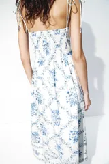 Vestido midi de popelina de algodón en color blanco con estampado floral azul, escote corazón y tirantes finos de lazo. Presenta cuerpo entallado, espalda elástica tipo nido de abeja y falda amplia con vuelo.