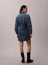 Vestido mini de denim azul con efecto desgastado, de manga larga, con cuello camisero, cierre frontal de botones metálicos y bolsillos con solapa en el pecho.