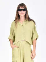 Camisa de corte cropped y holgado, color verde oliva, con cuello clásico, cierre frontal de botones y mangas cortas con dobladillo.