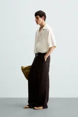 Camisa de calce relajado confeccionada en tejido de algodón color beige. Presenta un diseño de jacquard con líneas verticales desflecadas, cuello tipo bowling, manga corta y cierre frontal con botones.