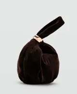 Bolso de mano pequeño confeccionado en terciopelo color marrón oscuro, con diseño fruncido y detalle de aro metálico dorado en el asa.