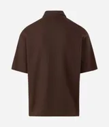 Remera polo de manga corta y corte regular, confeccionada en tejido texturizado color marrón, con cuello camisero, cartera corta con botones y un bolsillo aplicado en el pecho.