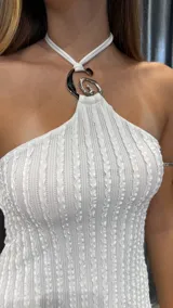 Vestido corto de color blanco con textura acanalada y diseño de cuello halter con detalle metálico circular en el centro. Presenta un corte ajustado al cuerpo y una caída fluida hacia el ruedo.