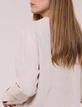 Camperita de tela liviana color beige, de silueta entallada con cuello a la base y abotonadura frontal con botones a tono. Cuenta con dos bolsillos con solapa en el frente, mangas largas con puños abotonados y largo a la cintura.