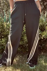 Pantalón deportivo color naranja con las icónicas tres rayas blancas laterales características de la marca Adidas.