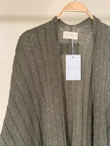 Ruana tejida de algodón con hilo lurex en punto jersey, color azul, con diseño amplio y detalle de etiqueta de cuerina en la parte posterior.