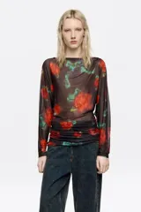 Camiseta de tul de manga larga con escote barco, diseño ajustado y efecto fruncido en los laterales del bajo. Presenta un estampado de flores rojas sobre fondo oscuro.