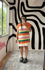 Vestido tejido a rayas horizontales de colores naranja, blanco, rosa, amarillo, verde y crudo, con mangas cortas y terminación con volados.