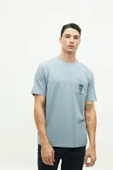 Remera celeste de manga corta con bolsillo en el pecho y estampado de palmera y texto en azul marino.