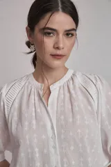 Camisa blanca con estampado de cruces, cuello mao y mangas 3/4 con detalle de pliegues en los hombros. Cierre frontal con botones.