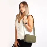 Bandolera rectangular color verde oliva, con correa ancha de tela regulable y logo metálico de la marca Korium en el frente.
